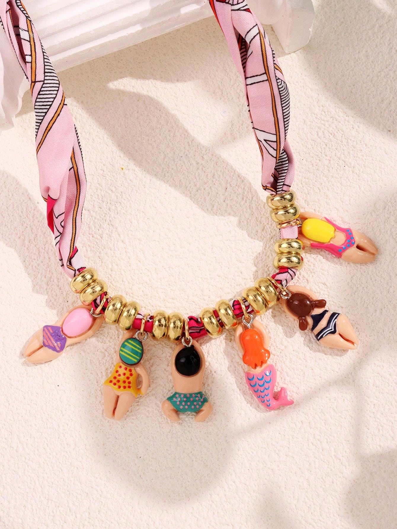 Necklace with colorful charms and a pink ribbon on a white background