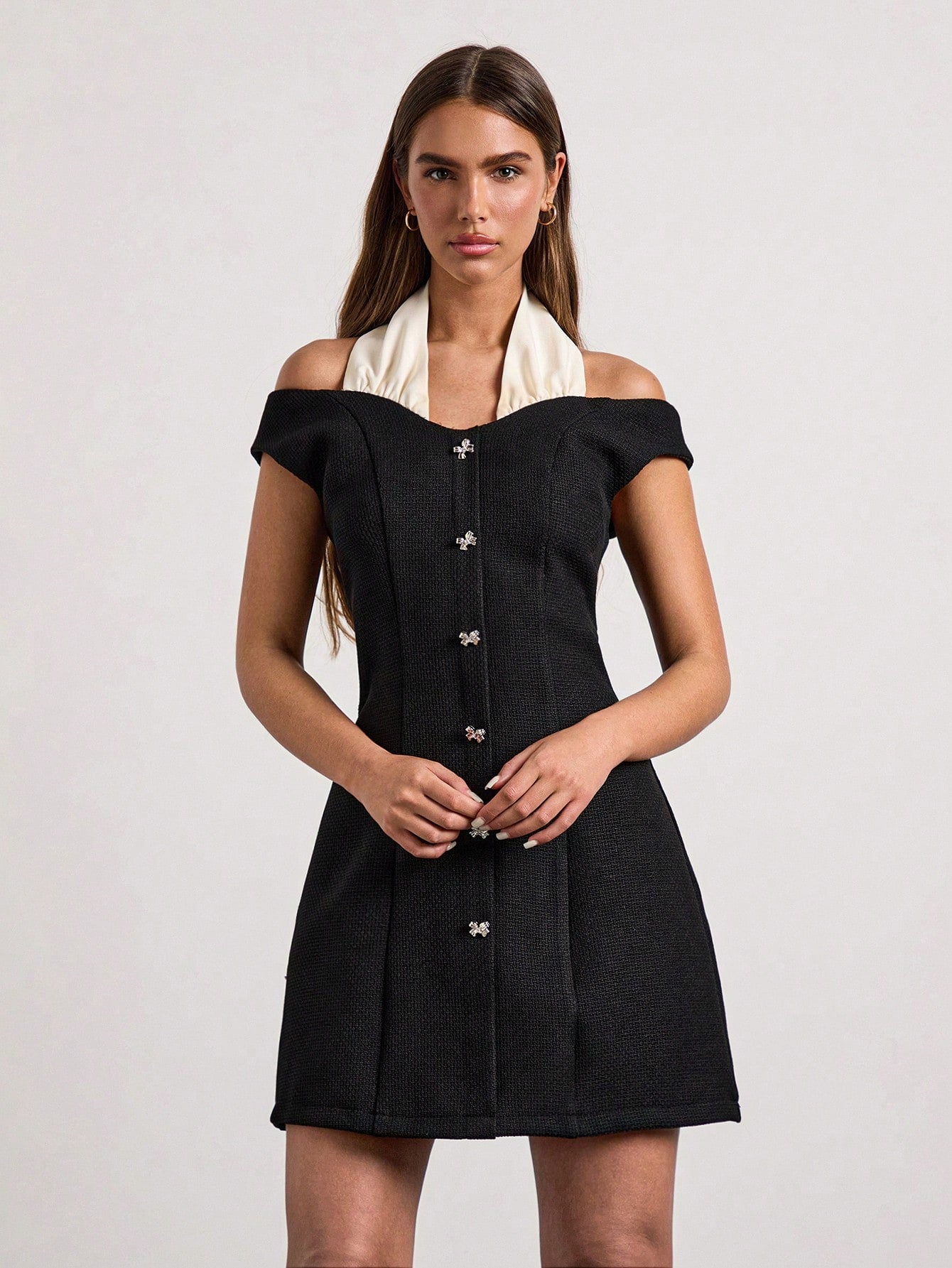 Woman wearing a black off-shoulder dress with a white collar against a light gray background