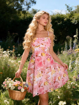 A woman stands in a sunlit flower field wearing a pink floral spaghetti-strap dress and holding a wicker basket of flowers.