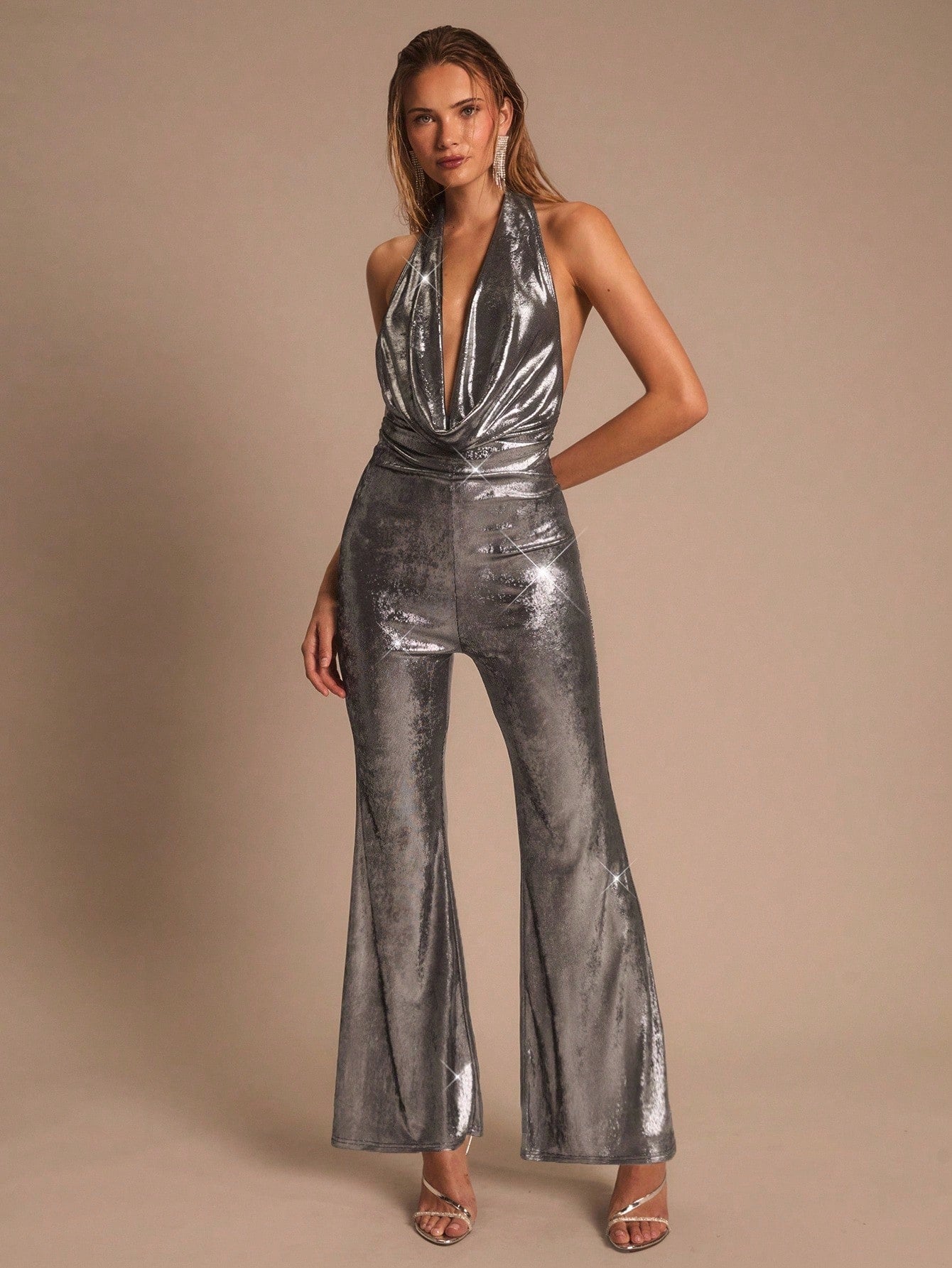 Woman wearing a metallic silver jumpsuit against a beige background