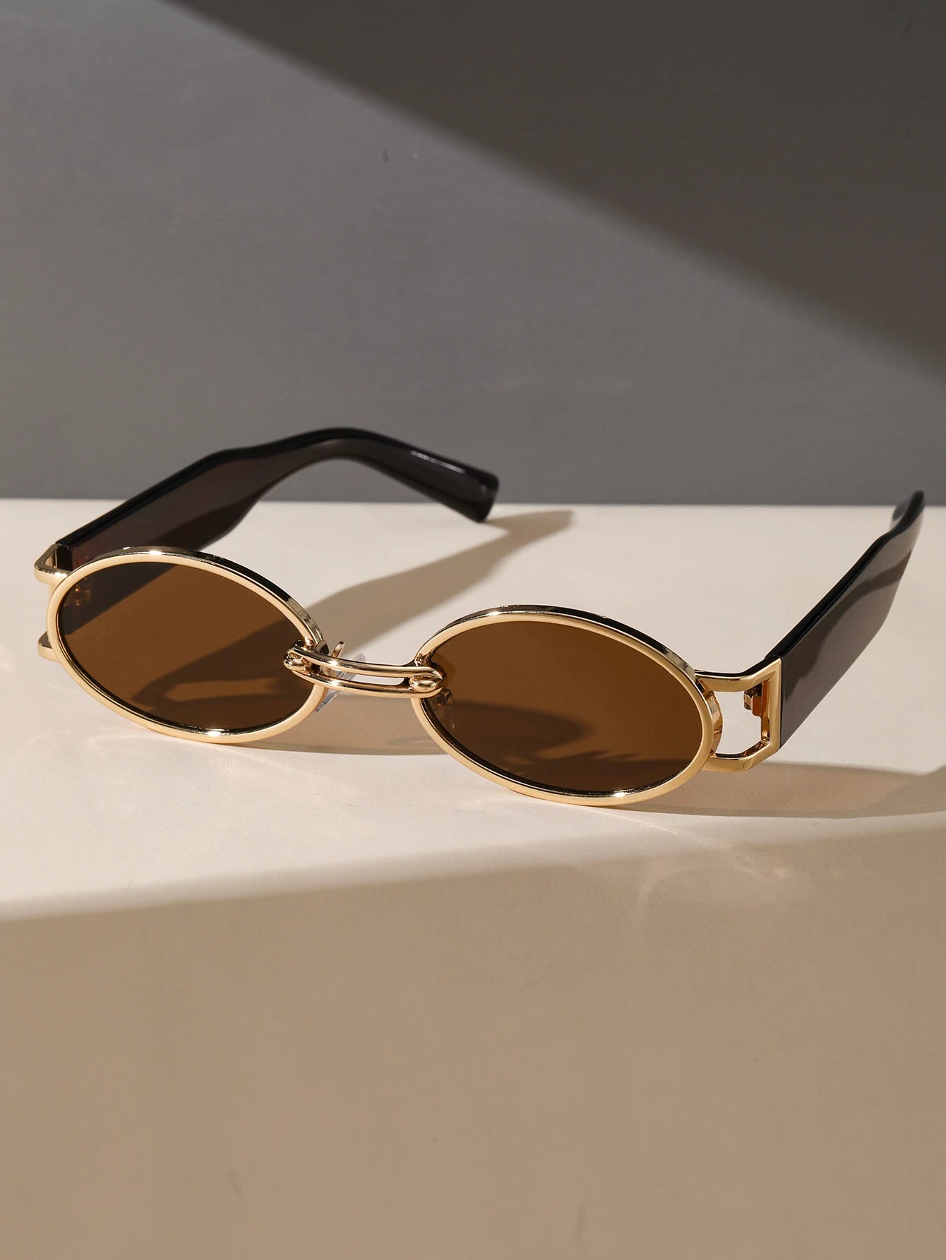 Sunglasses with gold frame and brown lenses on a light surface with a dark background