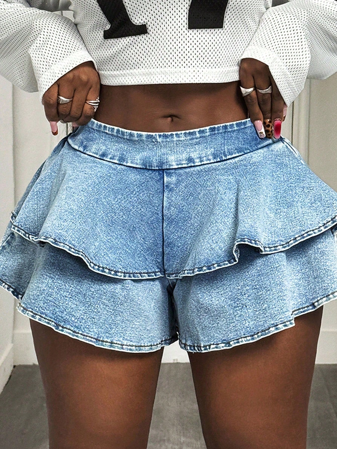 Person wearing a white mesh top and blue denim shorts with ruffled layers.