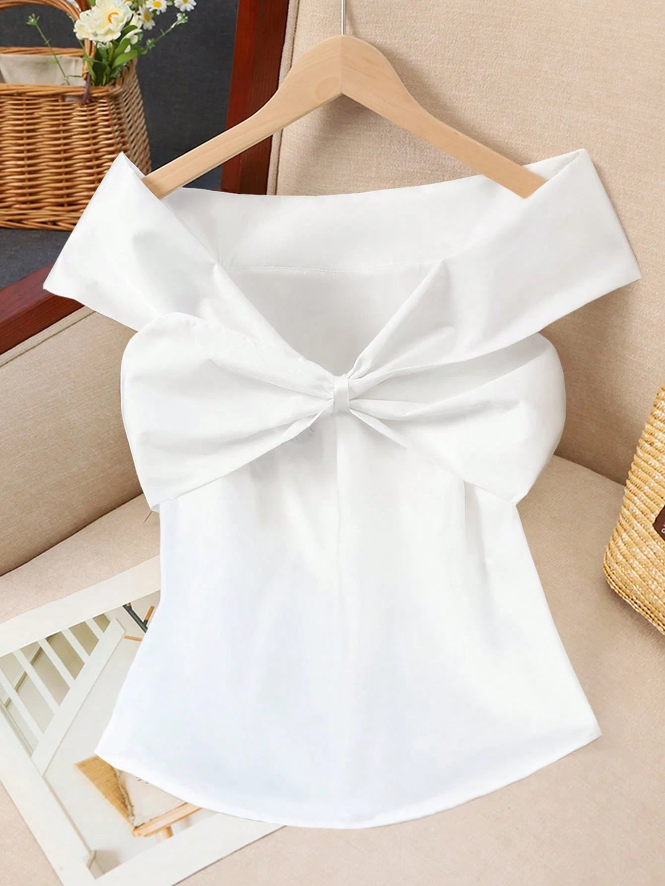 White off-shoulder top with a large bow on a hanger against a neutral background