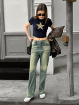 Woman in black top with star design and light blue jeans standing on a sidewalk.