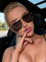 Woman wearing sunglasses and posing with a finger on her lips inside a car.
