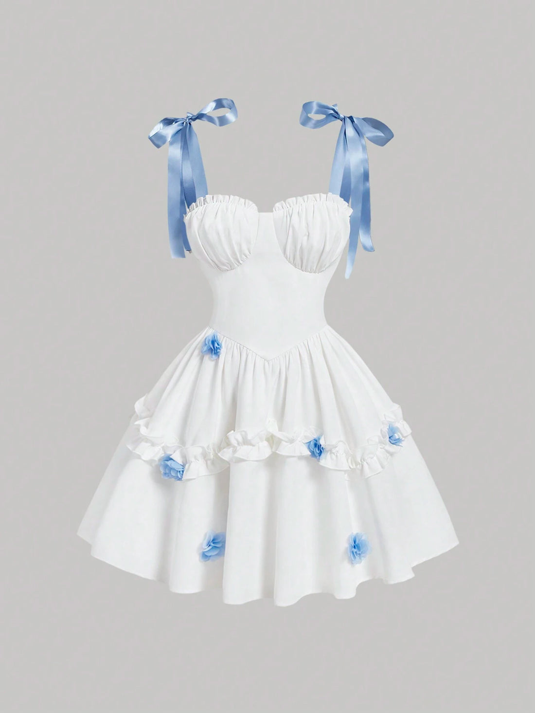 White strapless sweetheart dress with blue satin ribbon shoulder bows and blue fabric flower accents on a tiered skirt, shown against a solid gray background.