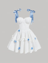 White strapless sweetheart dress with blue satin ribbon shoulder bows and blue fabric flower accents on a tiered skirt, shown against a solid gray background.