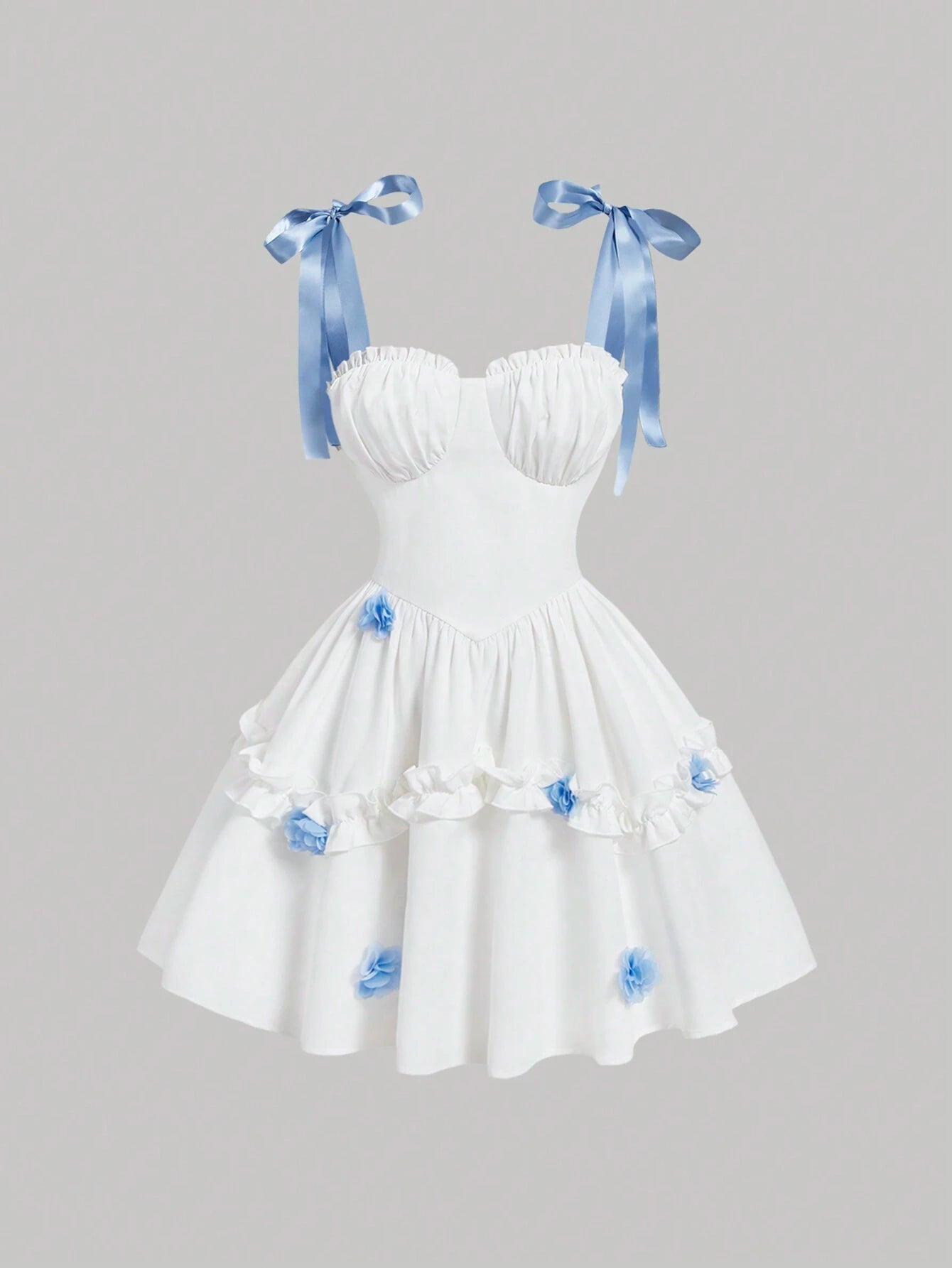 White strapless sweetheart dress with blue satin ribbon shoulder bows and blue fabric flower accents on a tiered skirt, shown against a solid gray background.