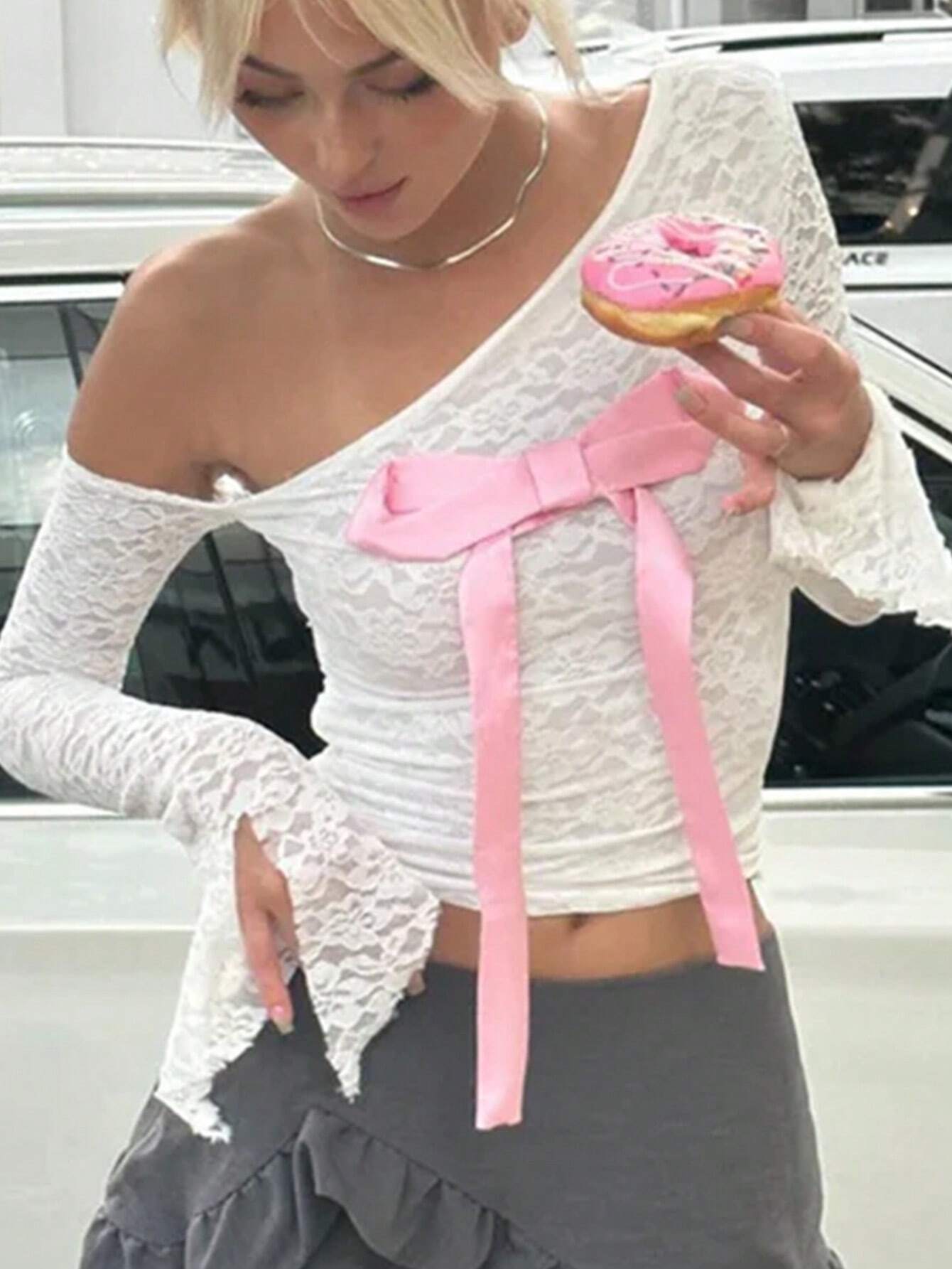 Woman wearing a white lace top with pink bows and holding a pink donut.