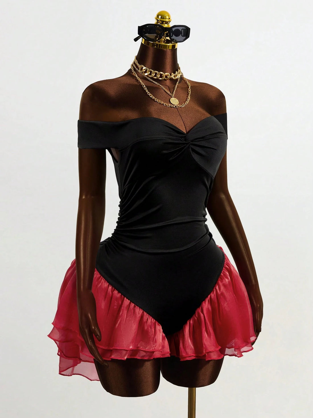 Mannequin wearing a black off-shoulder top and pink skirt with gold accessories on a white background
