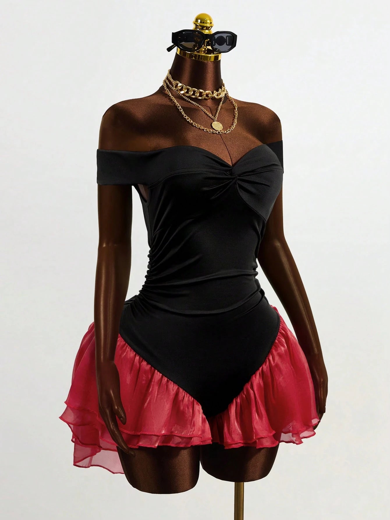 Mannequin wearing a black off-shoulder top and pink skirt with gold accessories on a white background