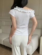 Person wearing a white textured top with ruffled shoulders in a room.
