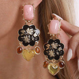 Close-up of a person wearing floral and heart-shaped earrings with pink, black, and gold colors.