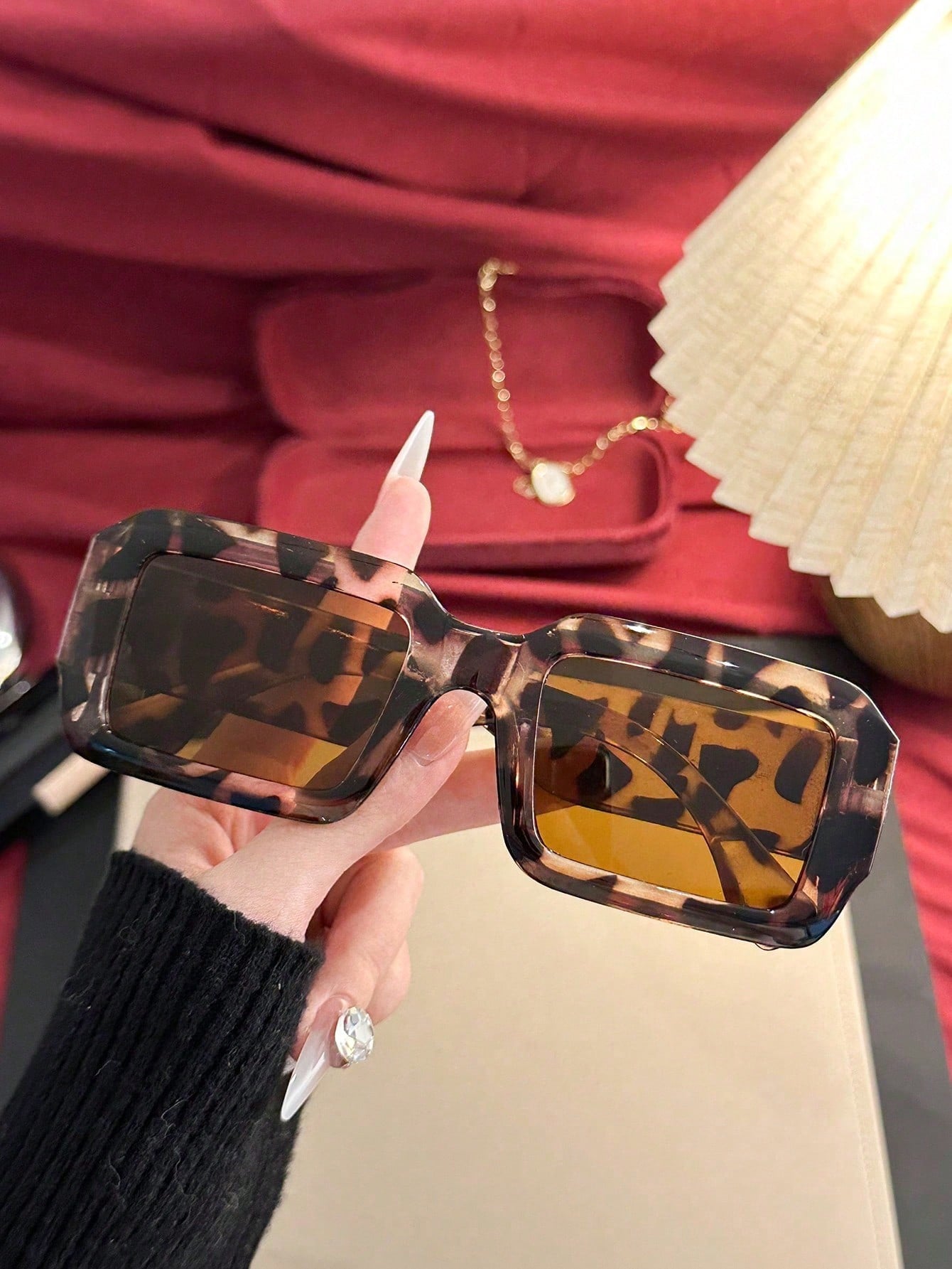 Person holding tortoiseshell sunglasses with a red interior background
