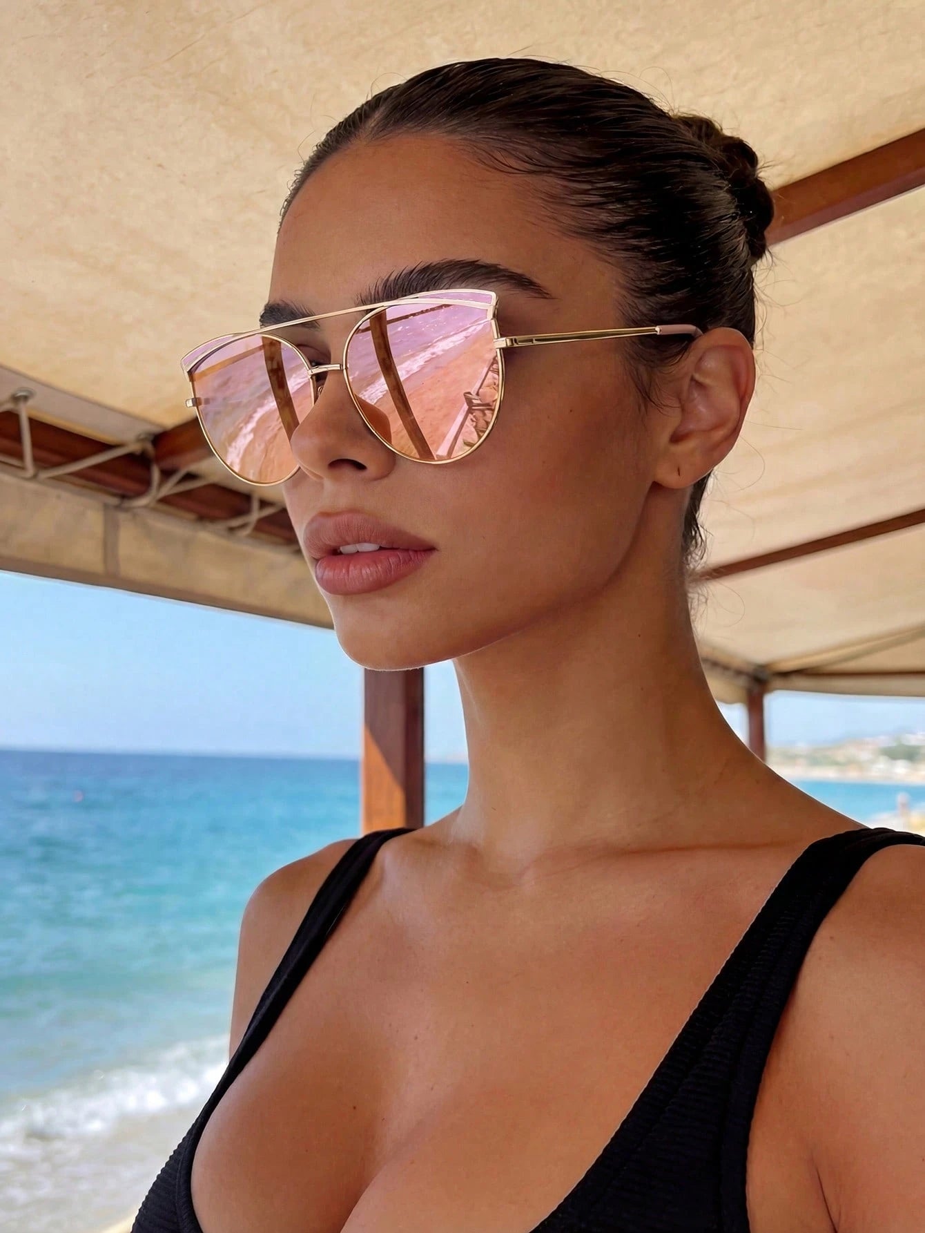 Woman wearing pink sunglasses and a black swimsuit by the beach