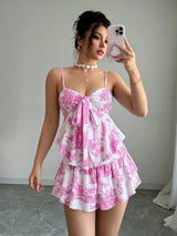 A woman takes a mirror selfie wearing a pink and white toile-patterned mini dress with spaghetti straps, a large bow at the bust, and a ruffled tiered skirt.
