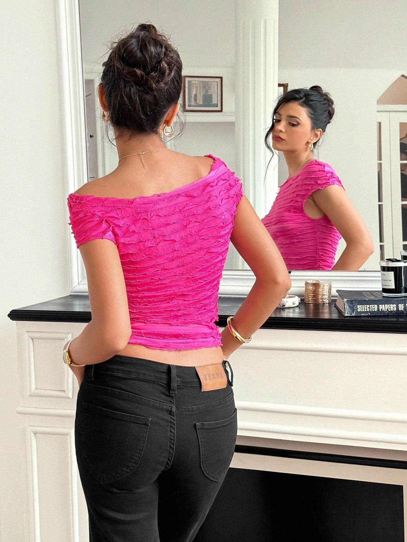 Woman wearing a bright pink top and black pants, standing in front of a mirror.