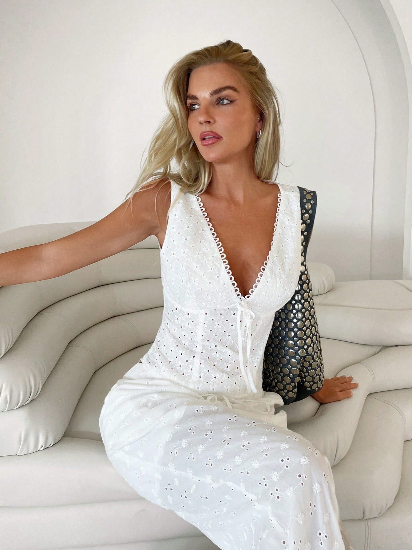 Woman in a white dress sitting on a white couch with a black handbag.