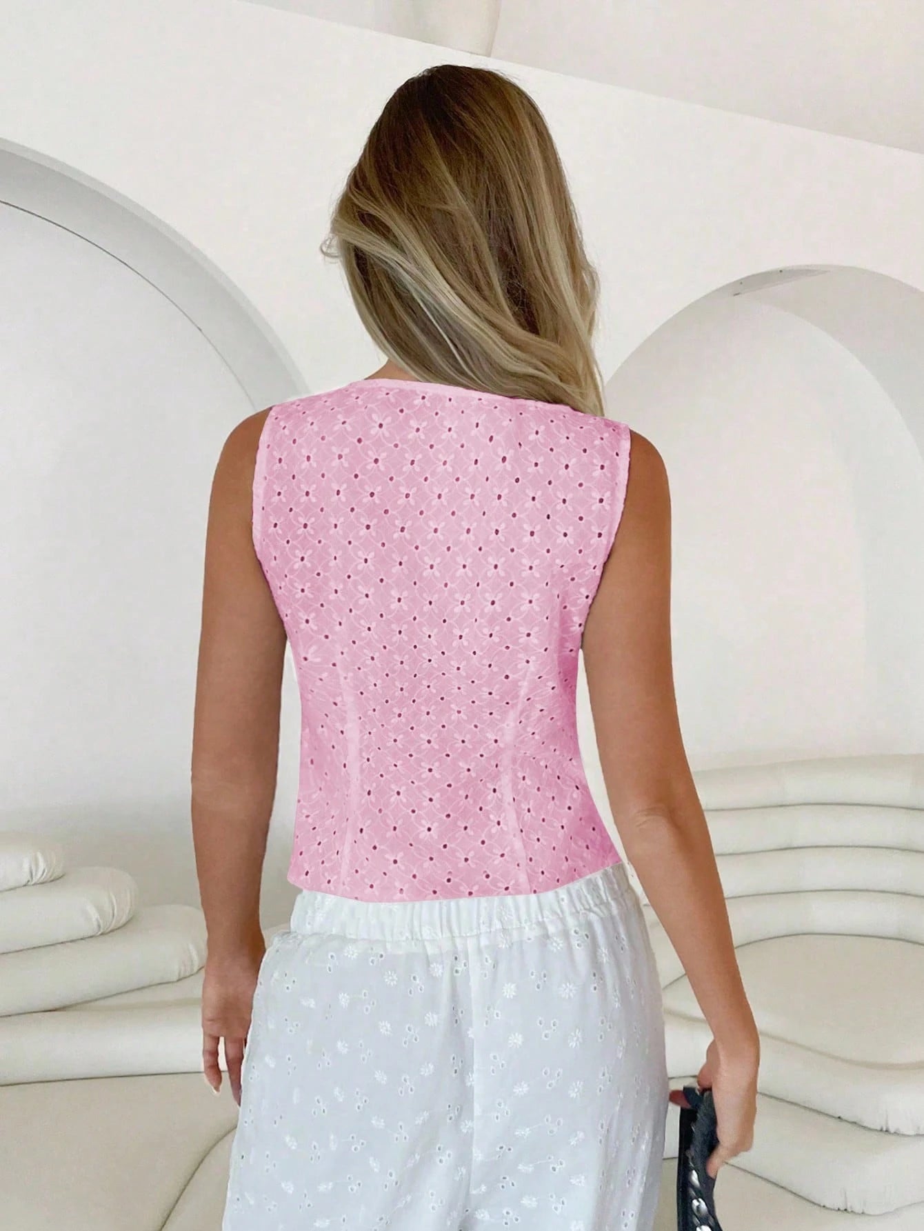 Woman wearing a pink top with white polka dots and white pants in a white room.