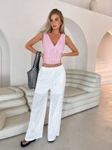Woman in pink top and white pants posing in a modern, light-colored interior.