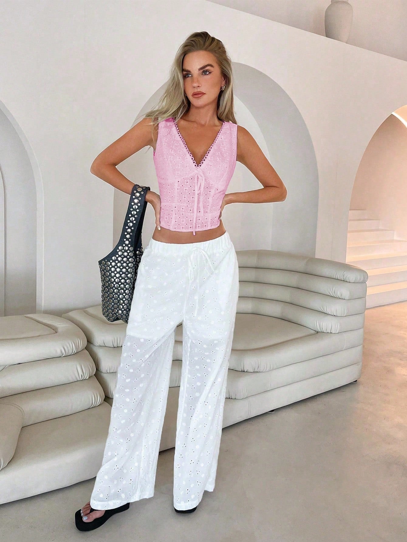 Woman in pink top and white pants posing in a modern, light-colored interior.