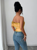 Woman wearing a yellow off-shoulder top and blue jeans against a plain background