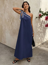 Woman wearing a blue dress with a white trim, standing against a textured wall with flowers.