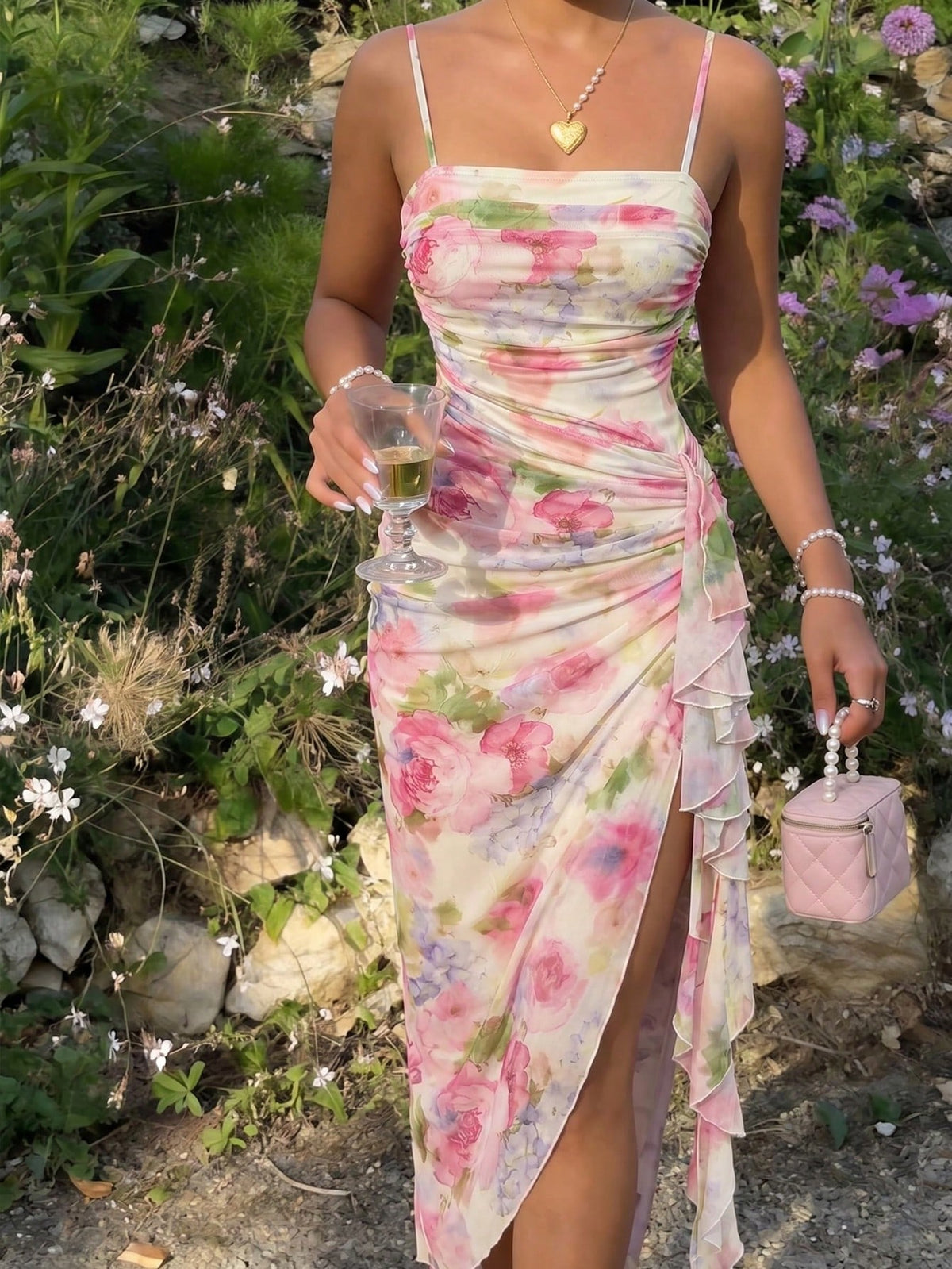Woman in a floral dress holding a glass and a pink handbag in a garden setting