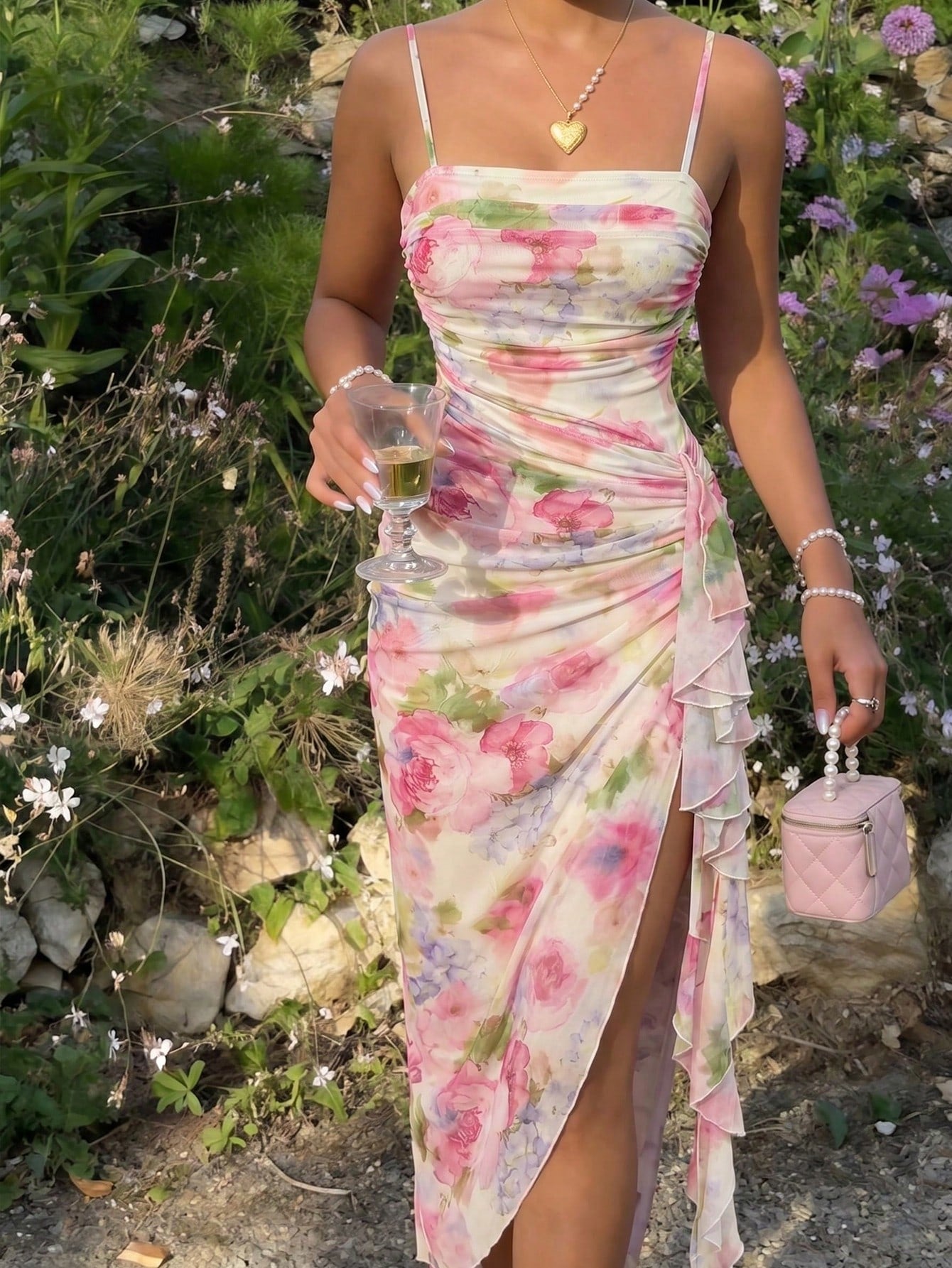 Woman in a floral dress holding a glass and a pink handbag in a garden setting