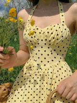 Person wearing a yellow polka dot dress holding flowers in a field