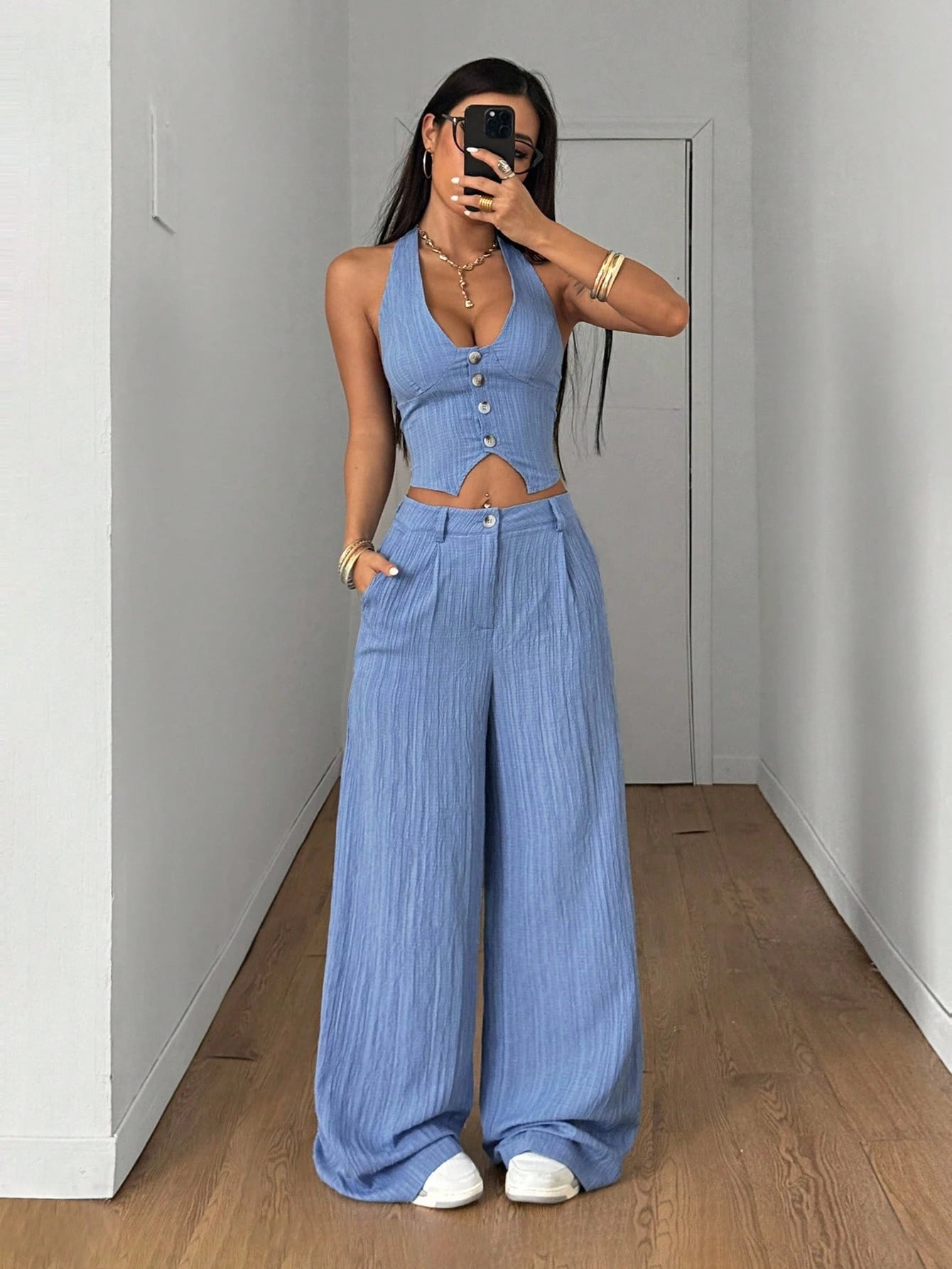 Woman wearing a blue outfit taking a mirror selfie in a room with wooden flooring.