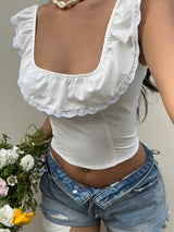 White lace-trimmed top worn by a person with denim shorts, holding flowers.