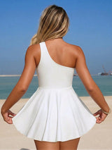 Woman in a white dress standing on a beach with clear blue sky and ocean.