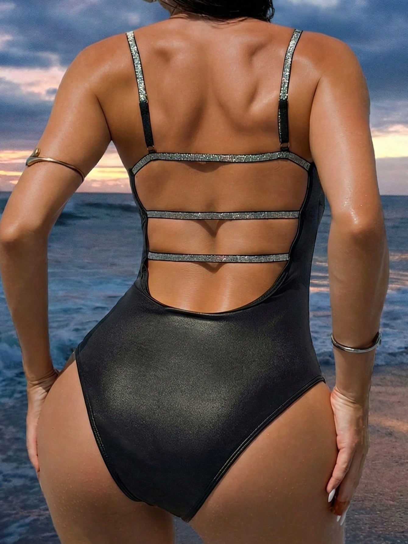 Person wearing a black swimsuit with cut-out design at the beach during sunset.