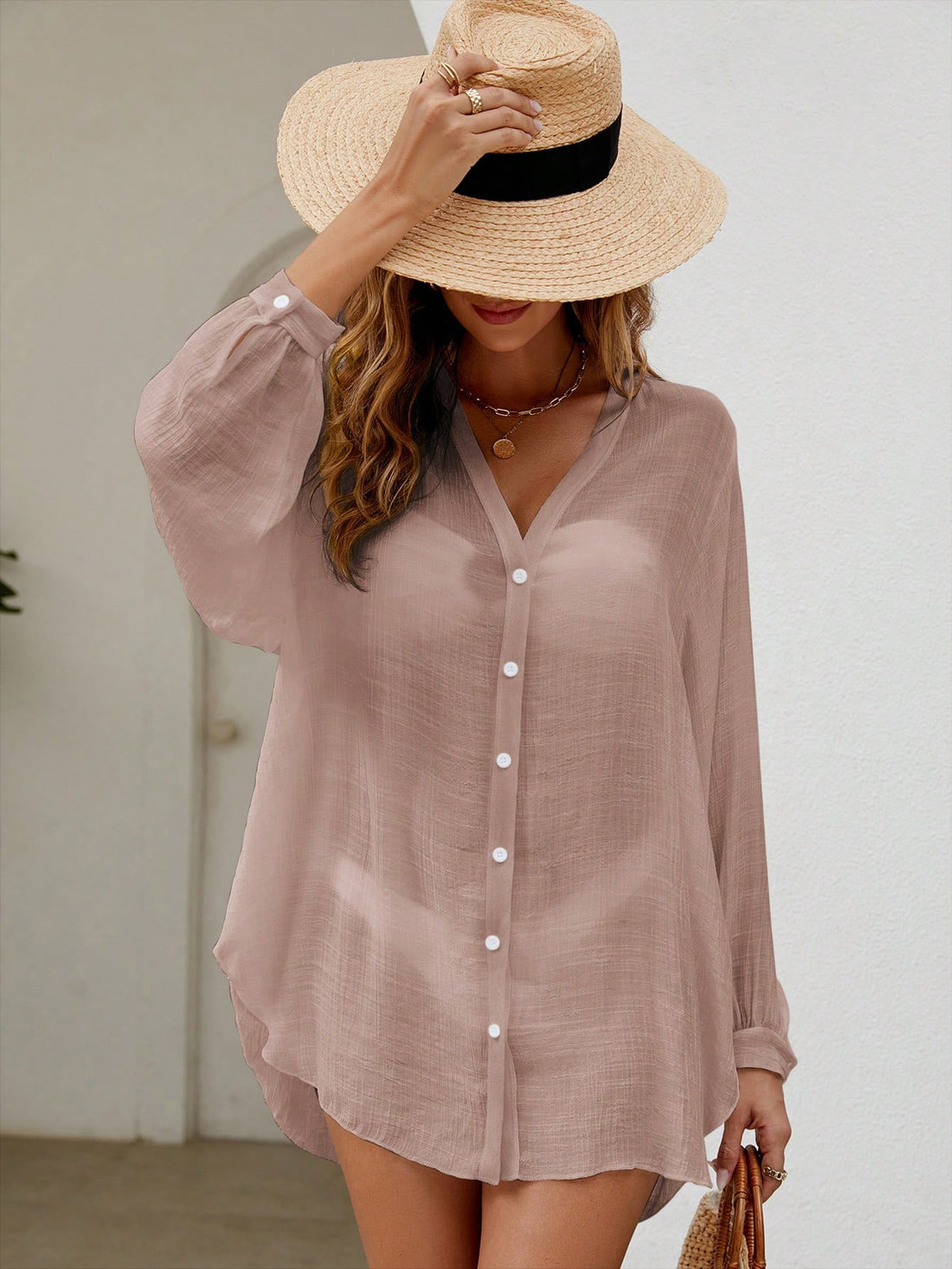 Woman wearing a light pink button-up shirt and straw hat indoors.