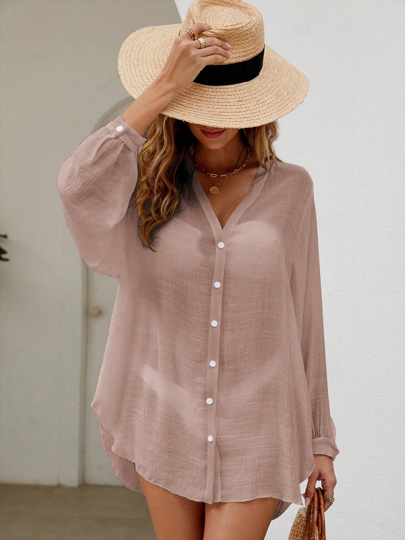 Woman wearing a light pink button-up shirt and straw hat indoors.