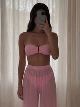 Person wearing a pink strapless top and pants against a neutral curtain background
