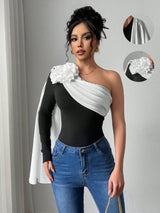 Woman wearing a black and white one-shoulder top with floral details and blue jeans.