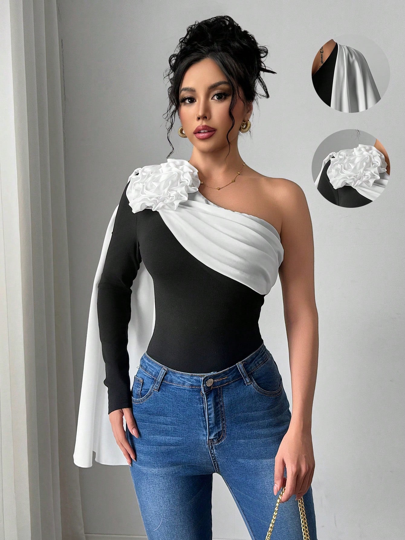 Woman wearing a black and white one-shoulder top with floral details and blue jeans.