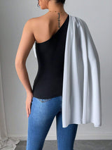 Person wearing a black one-shoulder top, blue jeans, and a white cape over their shoulder against a gray background.