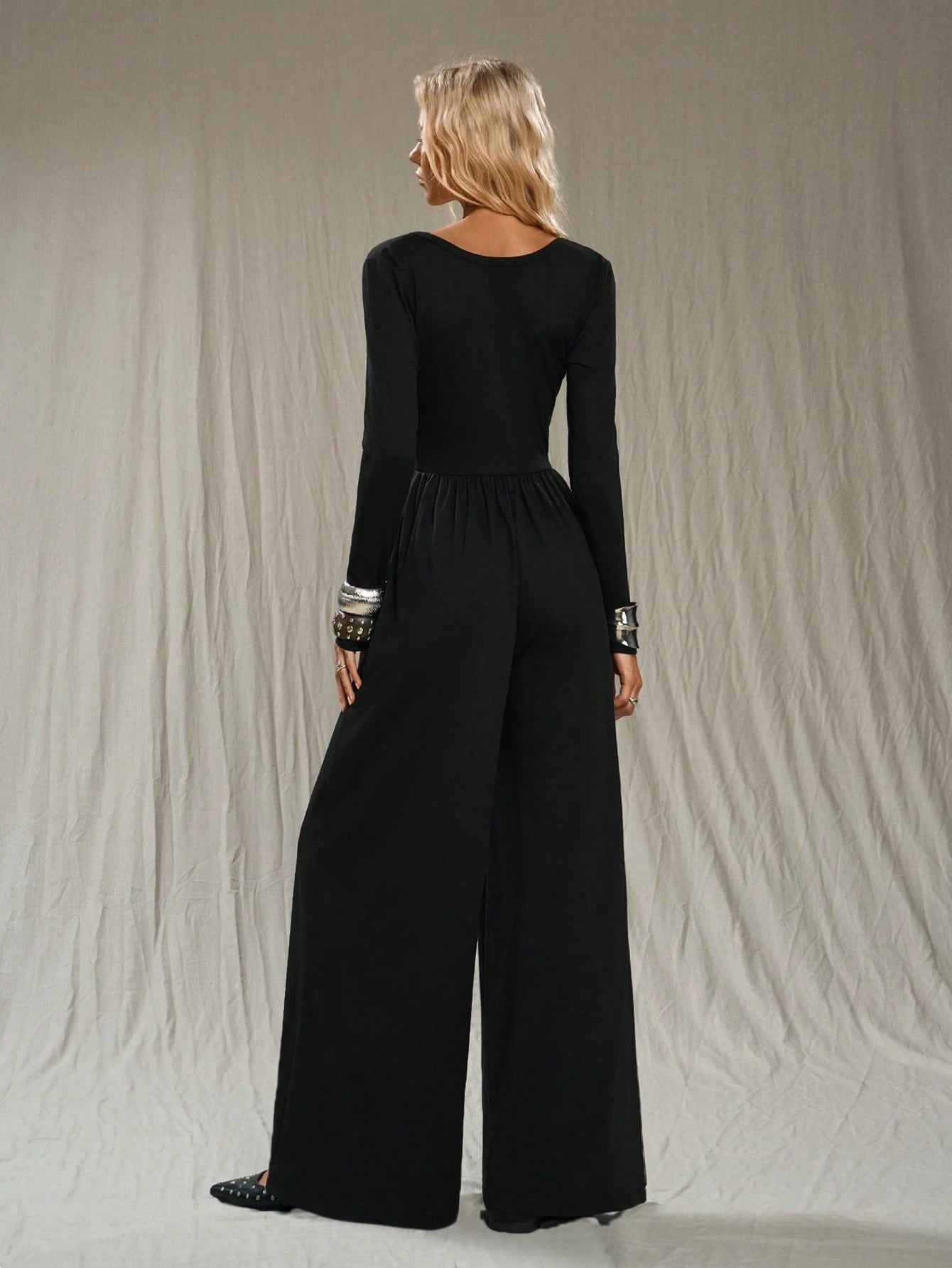 Woman wearing a black jumpsuit with long sleeves and wide-leg pants against a neutral background