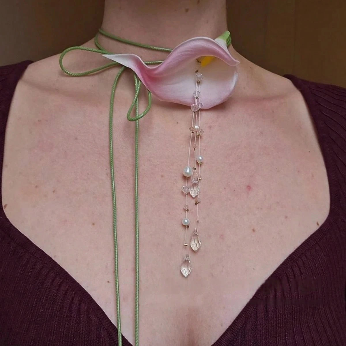 Necklace with a pink flower pendant and pearl-like beads on a person wearing a dark purple top.