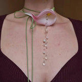 Necklace with a pink flower pendant and pearl-like beads on a person wearing a dark purple top.