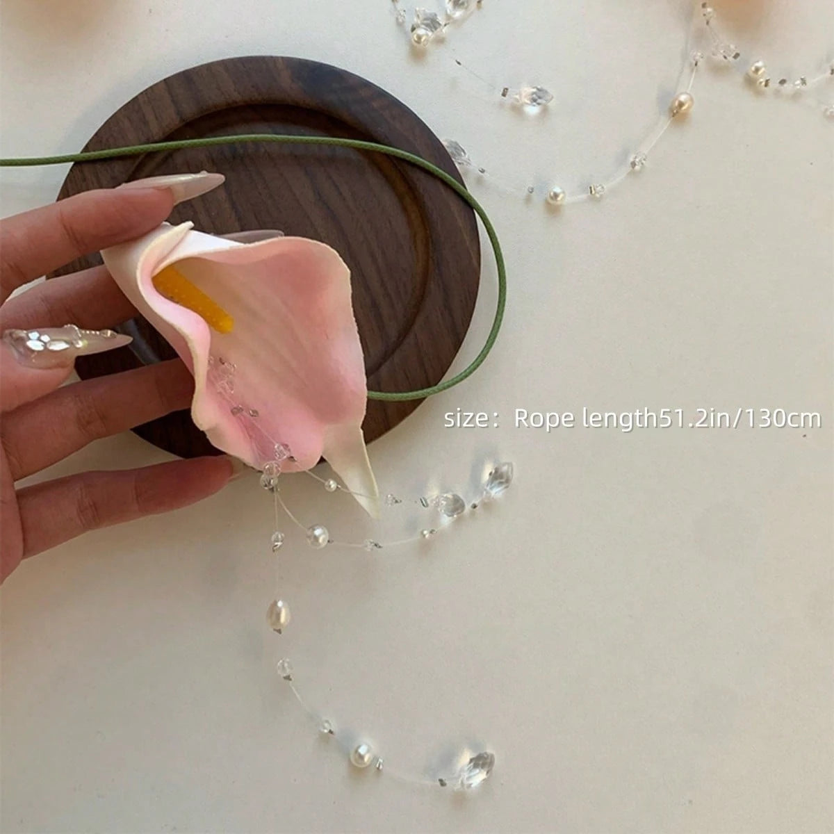 Hand holding a pink flower with a decorative string of pearls on a light background
