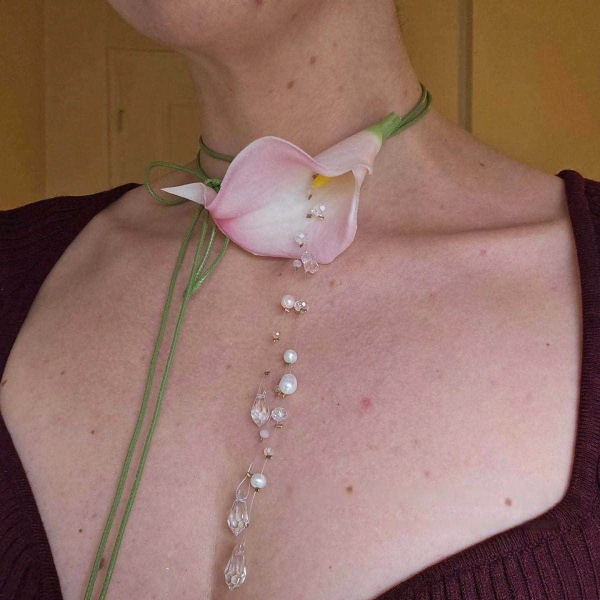 Necklace with a pink flower and beads worn by a person against a yellow background