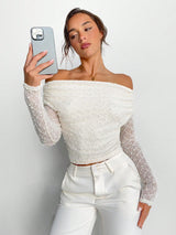 Woman wearing a white off-shoulder top with sheer sleeves against a plain background