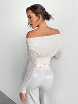 Woman wearing a white off-shoulder top with sheer sleeves against a plain background