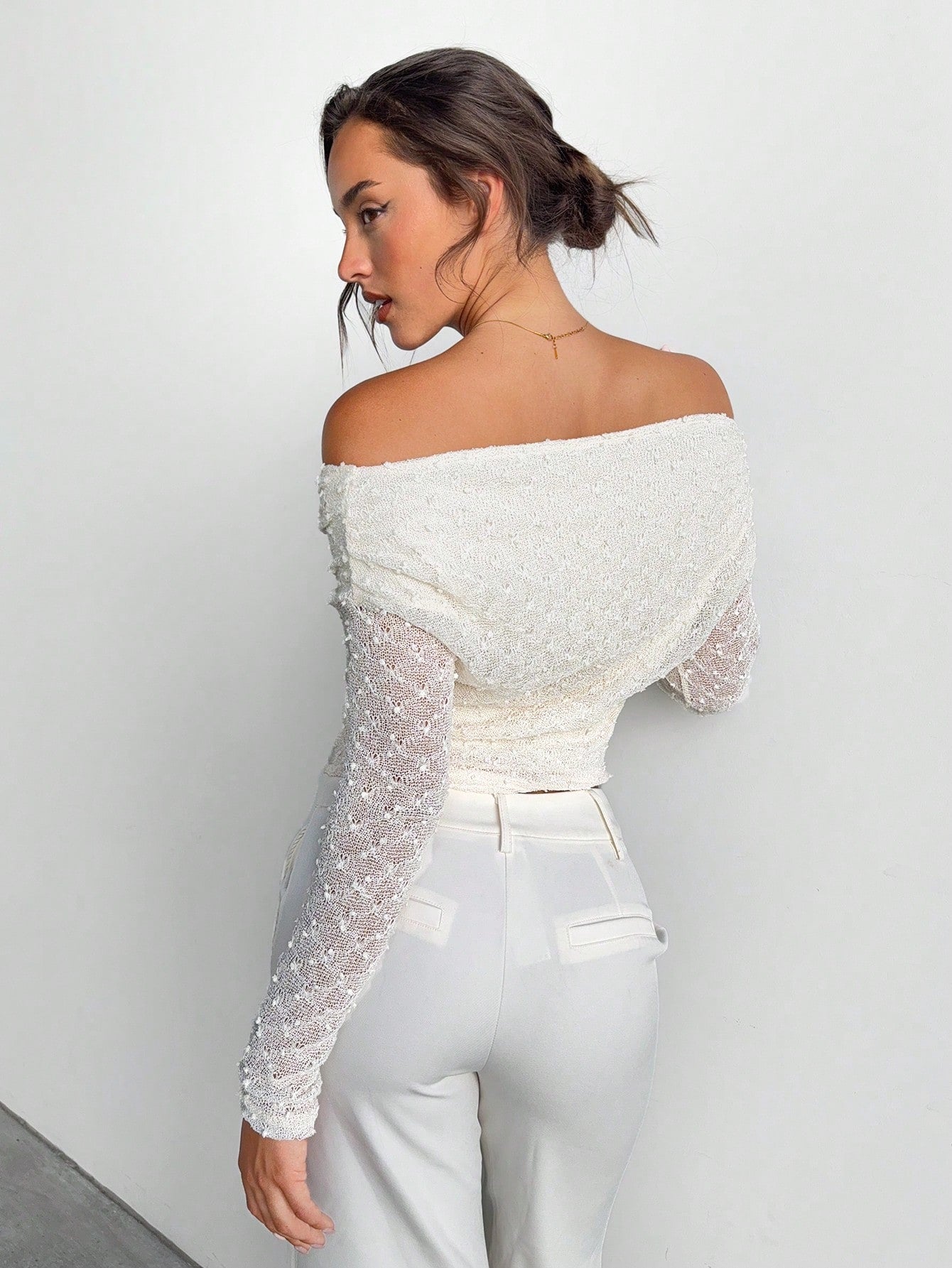 Woman wearing a white off-shoulder top with sheer sleeves against a plain background