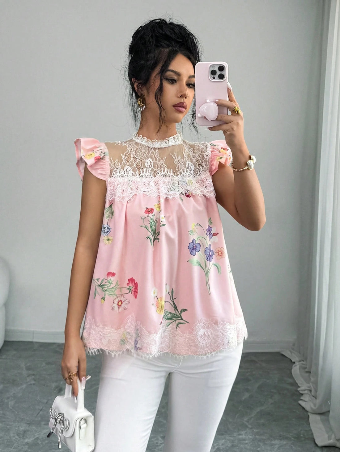 Woman taking a mirror selfie wearing a pink floral top with lace details.