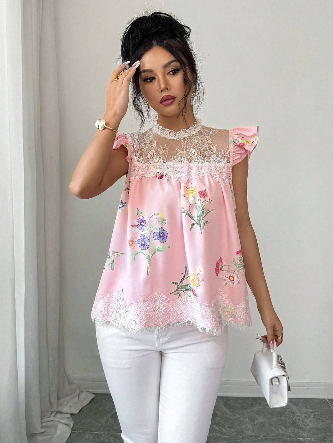 Woman wearing a pink floral blouse with white pants against a neutral background